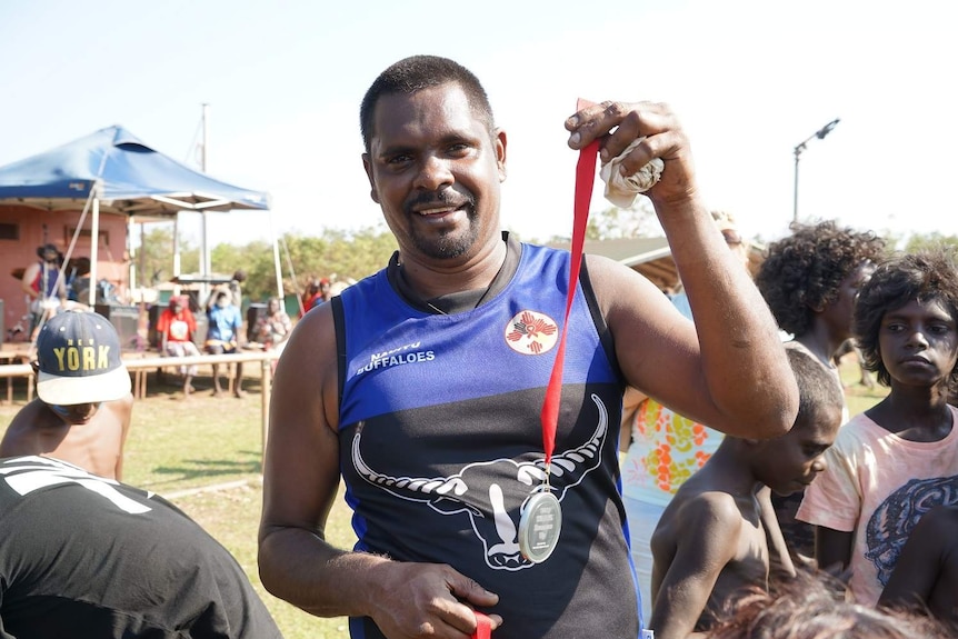 Jack Daly smiles and holds up a medallion in his Buffaloes footy jersey.
