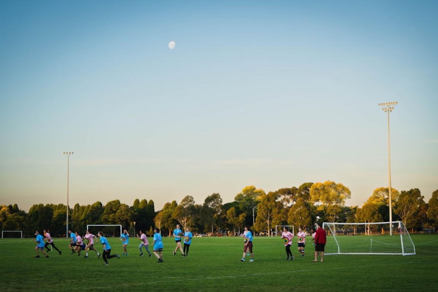 A wide shot of two teams playing a game of football as the sun is setting.