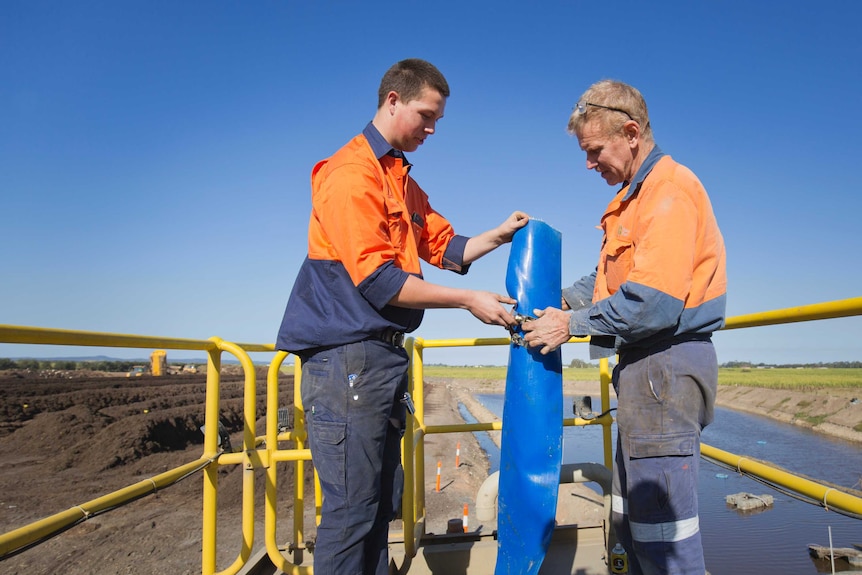 Two mechanics work together to fit some plastic piping on a platform overlooking windrows of compost.
