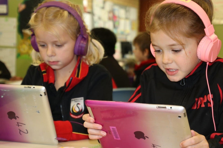 Two little girls sitting with headphones on looking at their lap tops