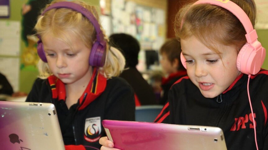 Two little girls sitting with headphones on looking at their lap tops