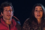 Andy Samberg and Cristin Milioti sitting in front of a campfire in Palm Springs