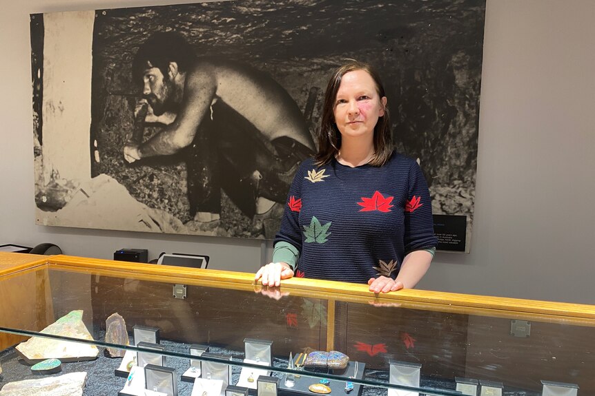 A woman standing behind a glass counter, with opals within.