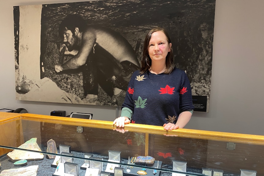 A woman standing behind a glass counter, with opals within.