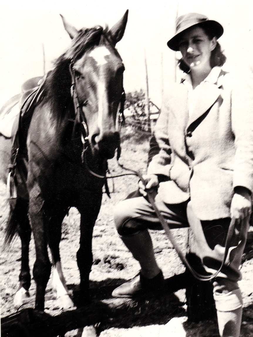 Black and white photograph of a woman in outdoor dress holding the reins of a horse.