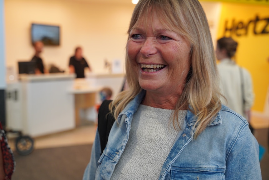 A middle aged woman smiles as she speaks to media inside an airport terminal building.