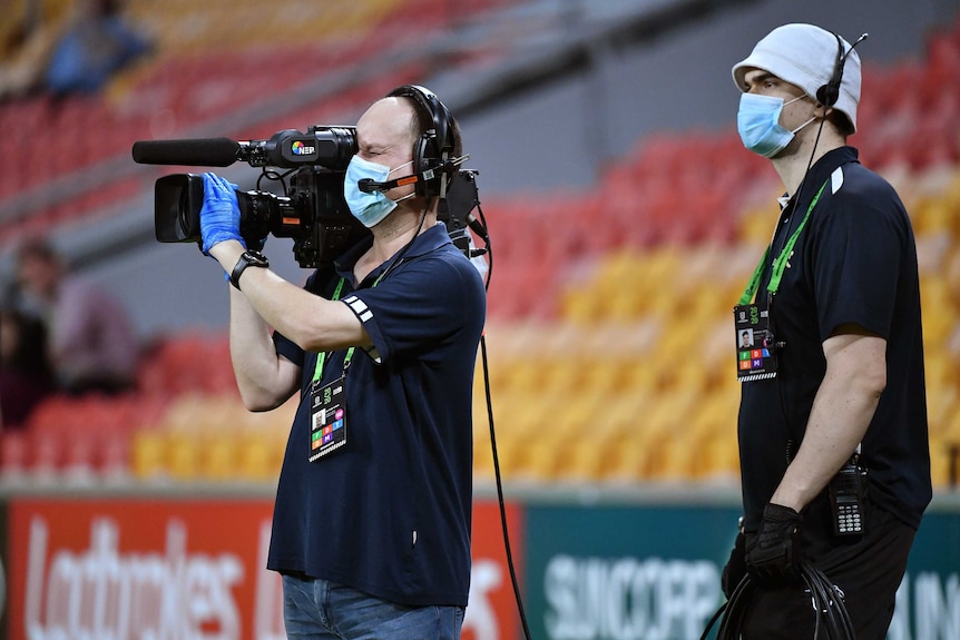 A camerman man and an assistant wear face masks at the NRL match between Brisbane Broncos and Parramatta Eels.