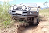 A 4WD leans to one side where a tyre is submerged in a deep pot hole on a dirt road.
