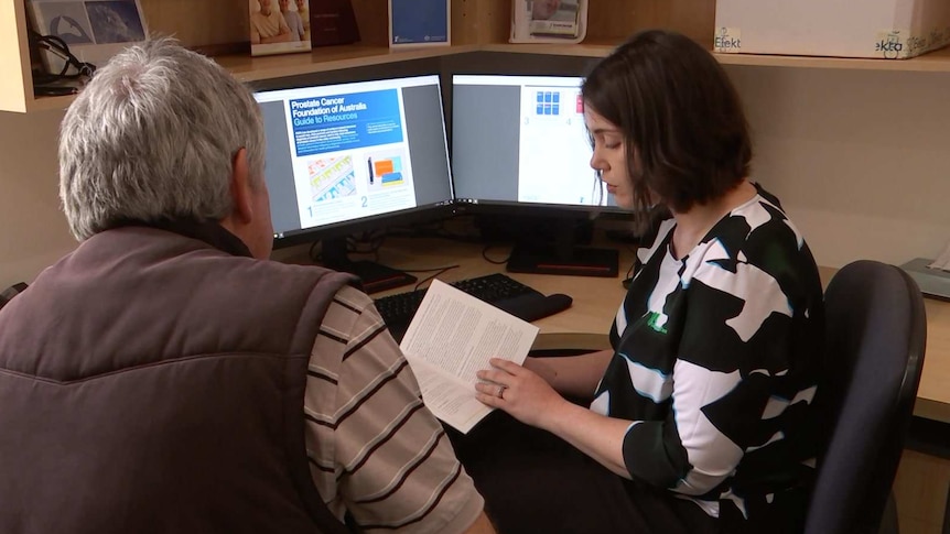 A woman holding a pamphlet in an office talks to a man