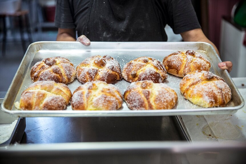 A man holds a tray of Pan de muerto, a traditional bread baked specially for Day of the Dead.