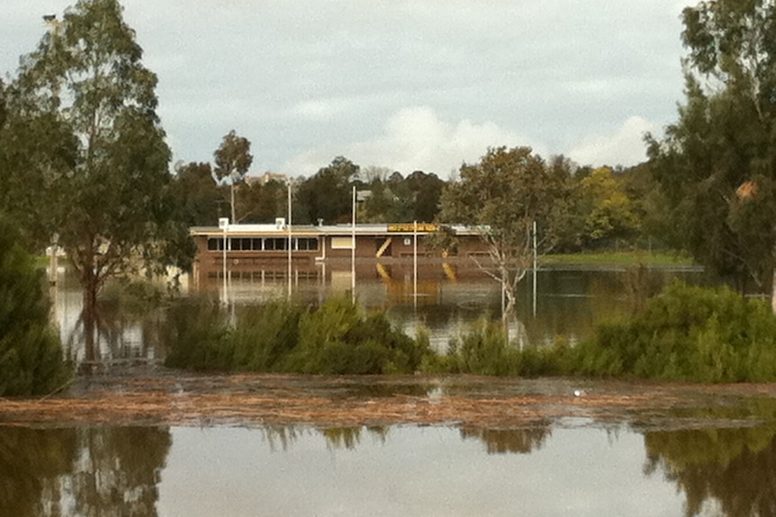 A brown brick sporting pavilion is flooded by a river.