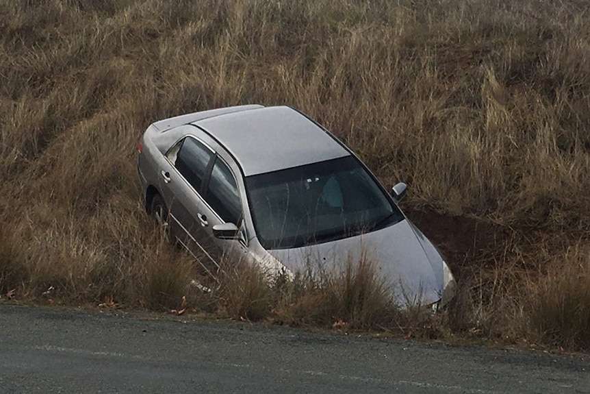 A silver car bonnet first in a ditch beside a road.