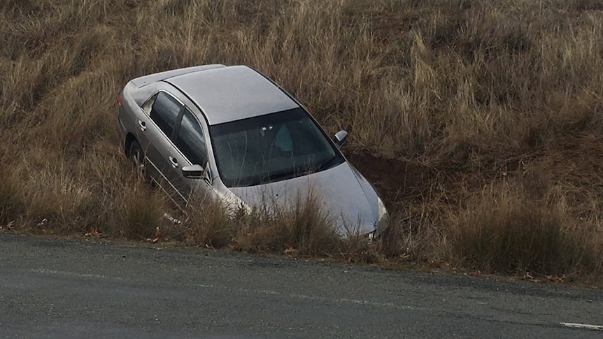 A silver car bonnet first in a ditch beside a road.