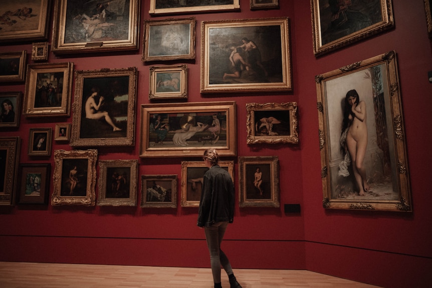 A woman looks at a wall of paintings.