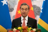 Wang Yi stands at a lectern in front of an Chinese and two Solomon Islands flags. 