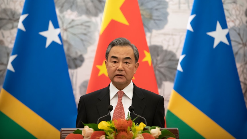 Wang Yi stands at a lectern in front of an Chinese and two Solomon Islands flags. 
