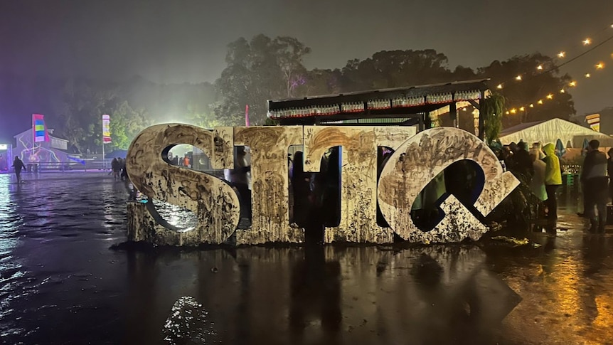Four big letters - S, I, T and G - at night, surrounded by dim lights and water, with the G falling over. 