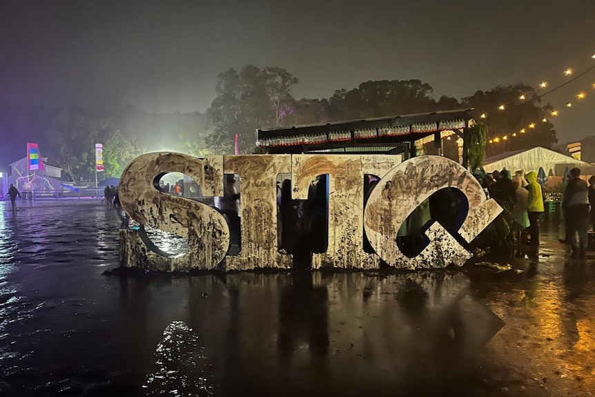 Four big letters - S, I, T and G - at night, surrounded by dim lights and water, with the G falling over. 