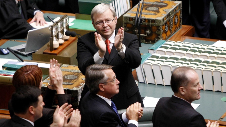 Kevin Rudd, in a dark suit stands with his back to the dispatch box and his hands raised to people unseen in lower house gallery