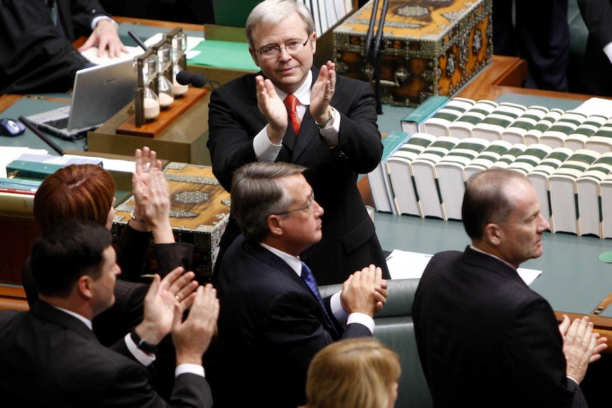 Kevin Rudd, in a dark suit stands with his back to the dispatch box and his hands raised to people unseen in lower house gallery