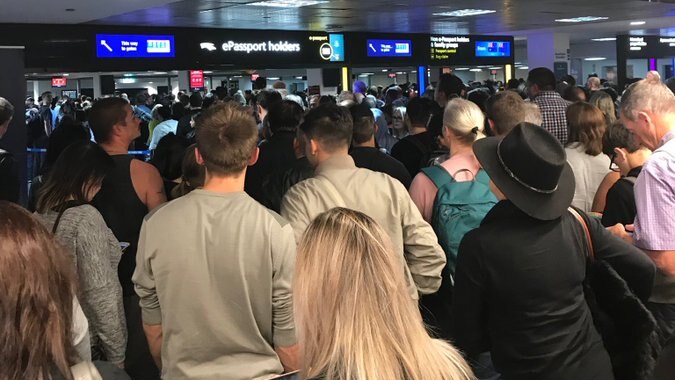 A large crowd of people stands in front of passport gates in an airport.