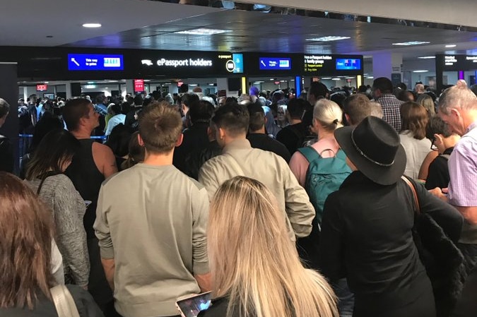 A large crowd of people stands in front of passport gates in an airport.