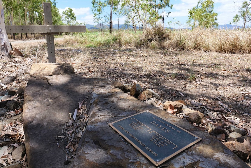 A marked lone grave under a pile of rocks beside a dirt road.