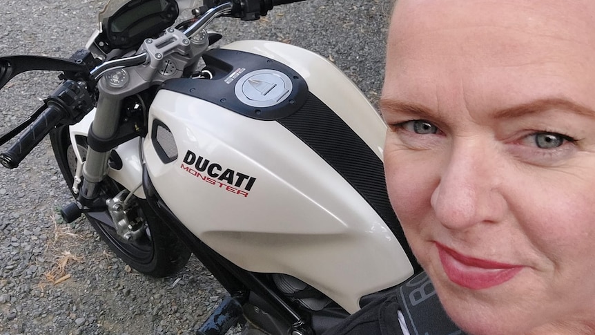 A ginger-haired woman takes a selfie near a Ducati motorcycle.