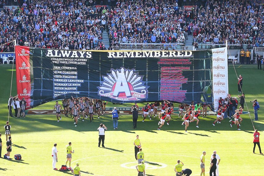 Collingwood and Essendon players run through the Anzac Day banner at the MCG on April 25, 2014.
