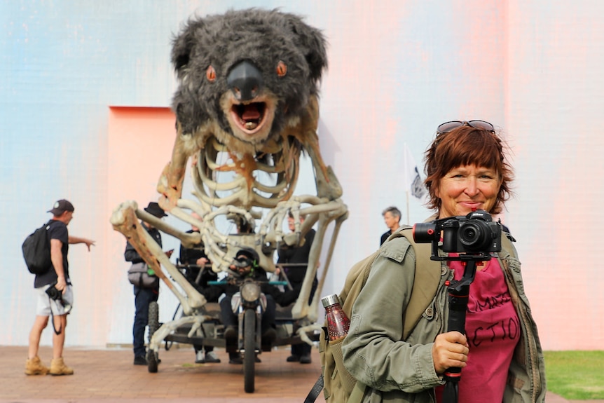 A young woman with a camera in front of a large koala puppet