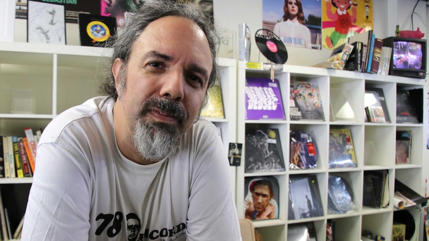Close-up of a man leaning on the counter of a record store with vinyl albums in the background.