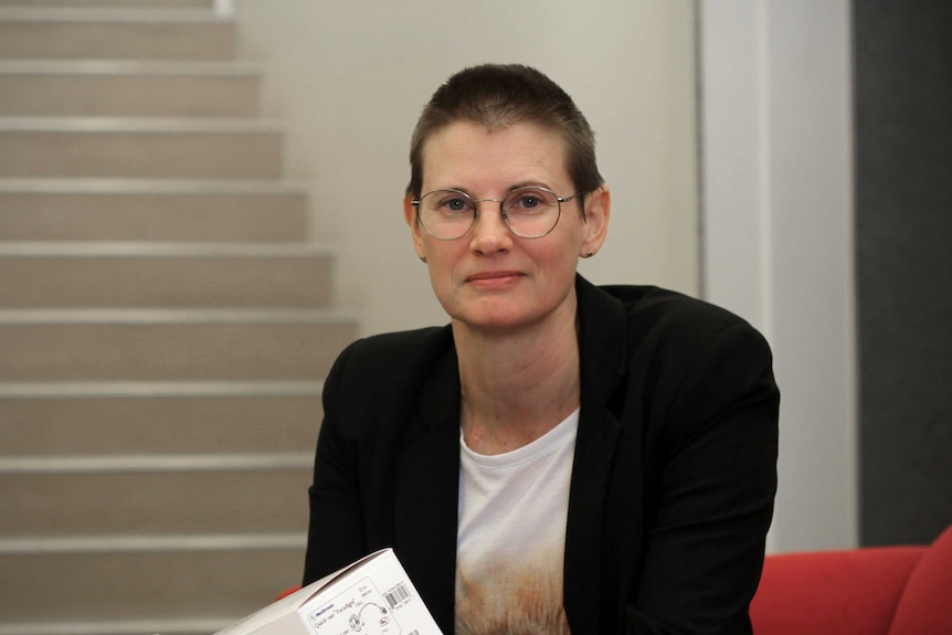 Dr Julie Mudd sits on a red couch in front of a stair case.