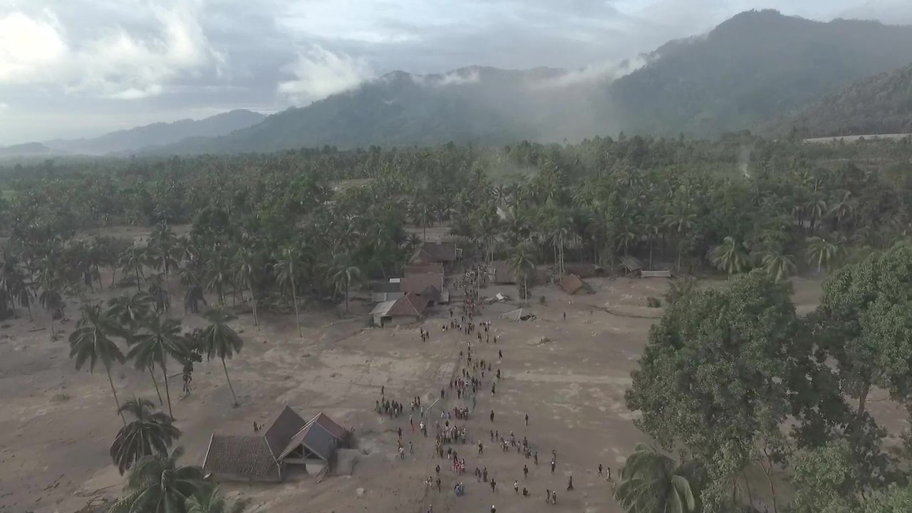 An image shows people streaming through a small village set in front of a volcanic mountain range
