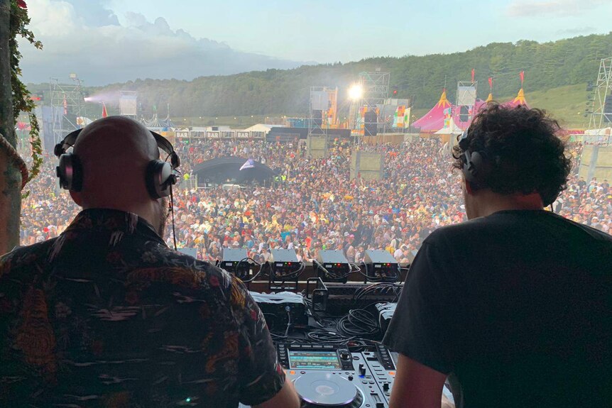 A large crowd seen from the stage behind two men who are DJs.