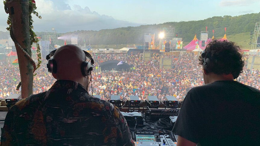 A large crowd seen from the stage behind two men who are DJs