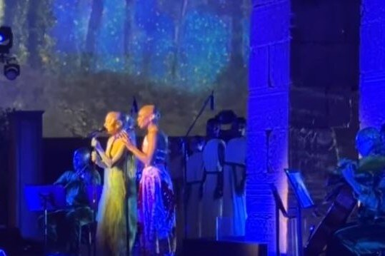 Two women standing on stage singing. 