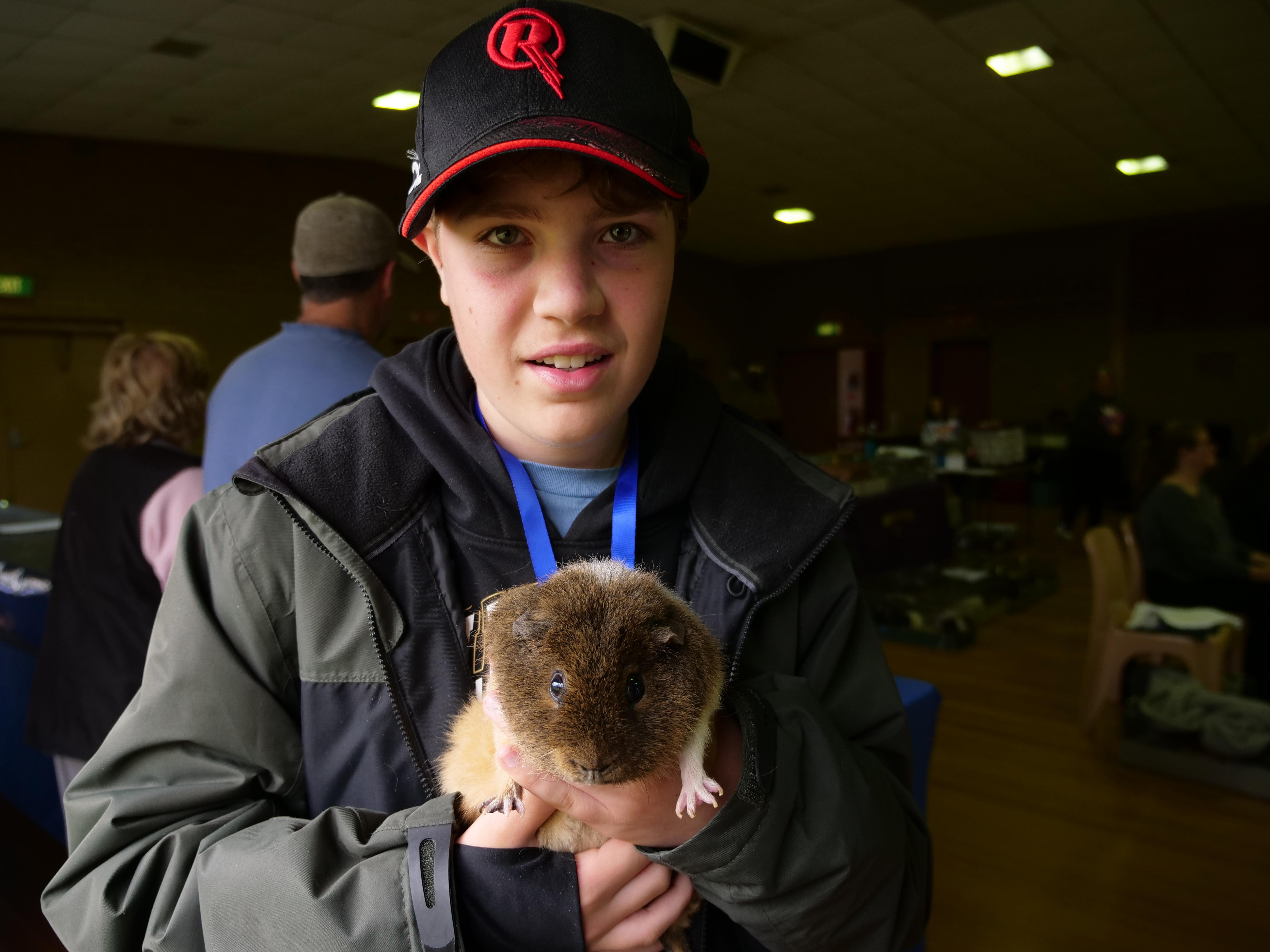 Um menino de boné sorrindo e segurando uma cobaia 