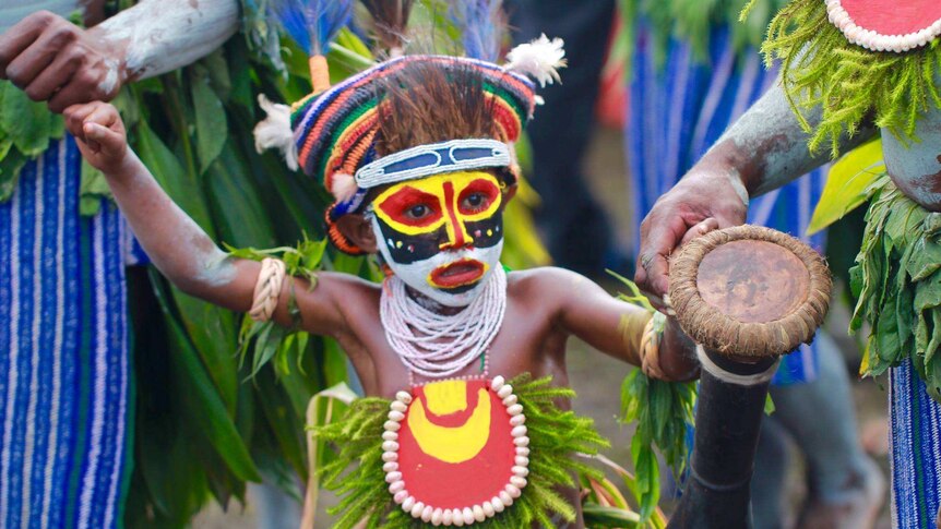 A child in red, white, yellow and black facepaint holding a Kundu drum at the 2016 Goroka Show, Papua New Guinea.