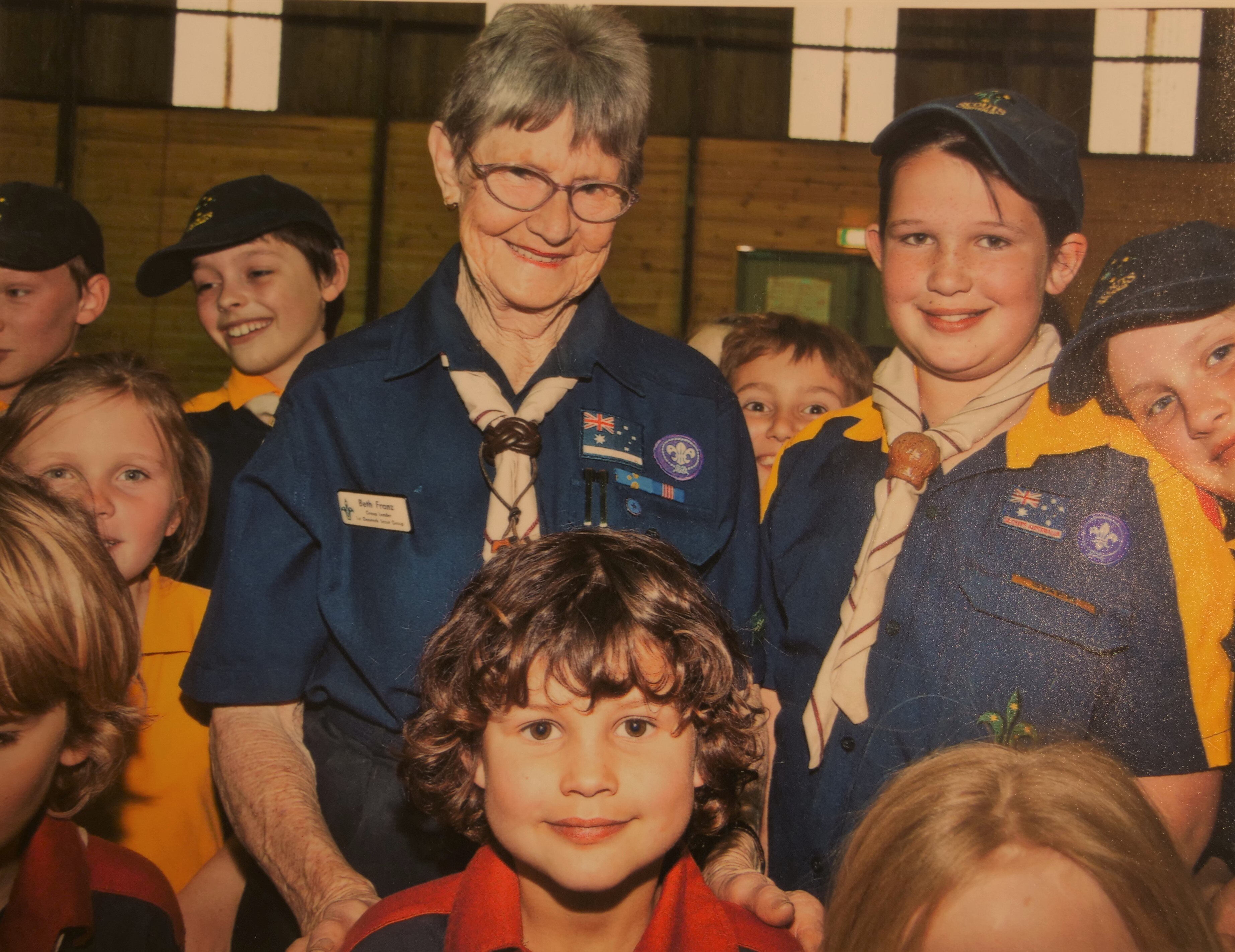 a woman standing with some kids, all are in yellow and blue scout uniforms.