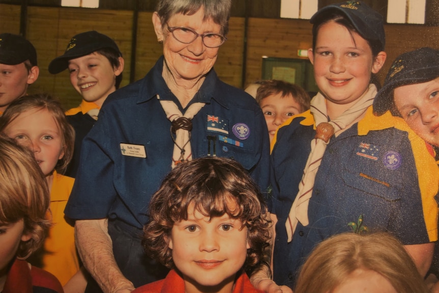 a woman standing with some kids, all are in yellow and blue scout uniforms.