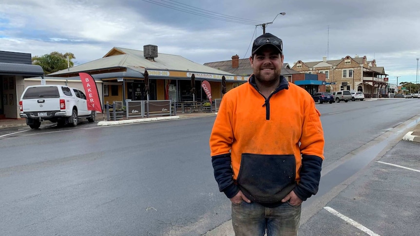 A man in a high-viz working vest stands in the main street of a rural town