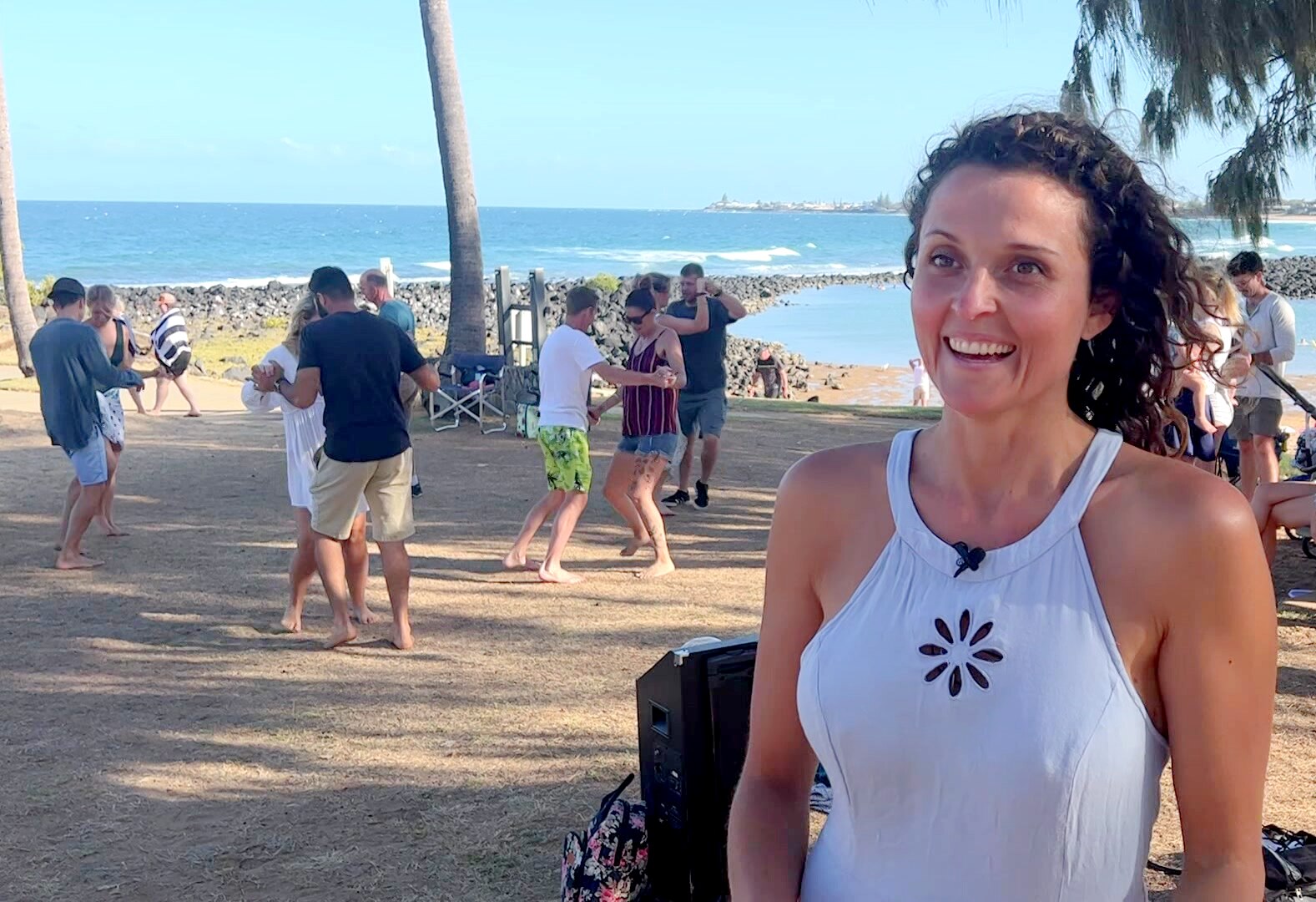 A woman looking just past the camera with a group of dancers and the beach behind her.