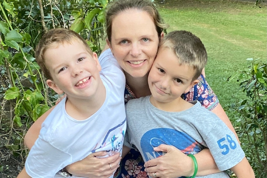 A woman standing with two small boys, smiling.