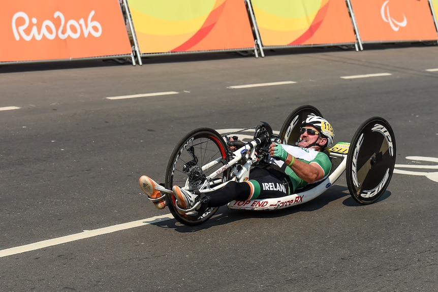  Paralympic athlete lies down in a handcycle, using a hand pump to propel himself during a time trial.