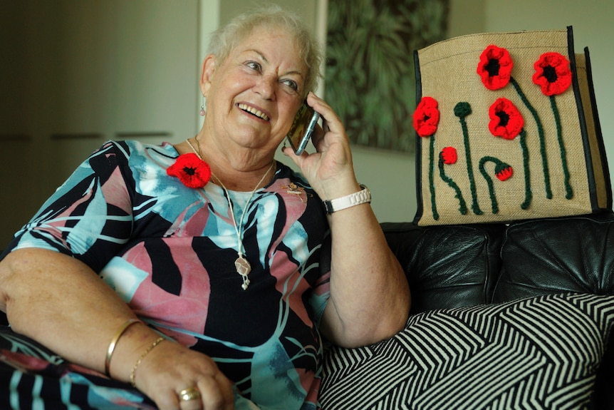 Older woman sits on a couch in a comfortable position, holding a mobile phone to her ear and smiling in a happy conversation.