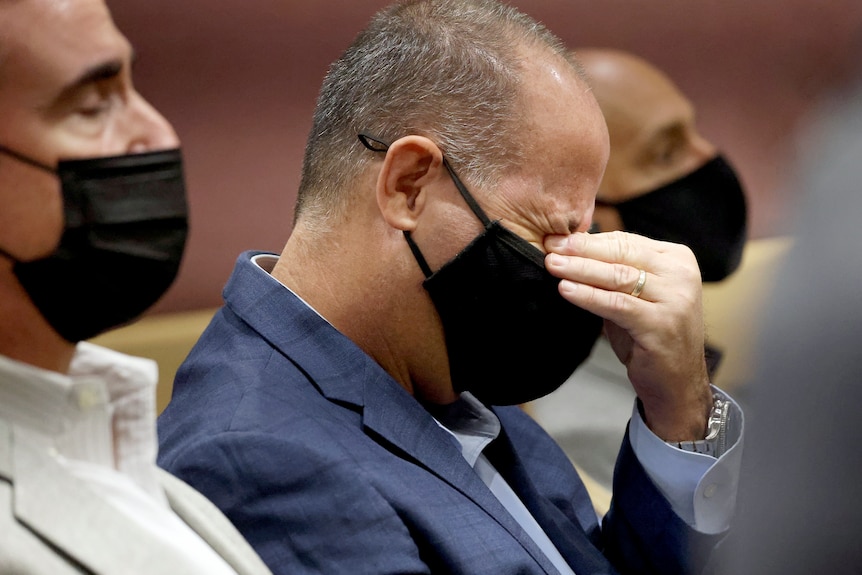 A man with a Cvid-19 mask places his hands over his eyes as he weeps on a court bench. 
