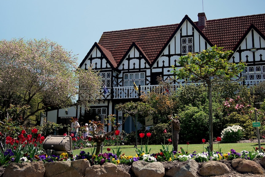 A line of people standing outside near flowers in front of a large ornate white building.