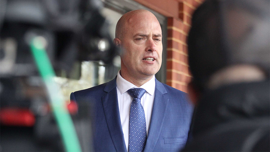 A mid shot of Dean Nalder talking in front of television cameras.