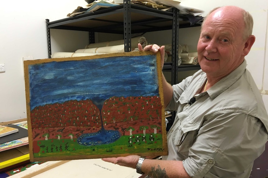 Greg Crofts holding a painting in a store room