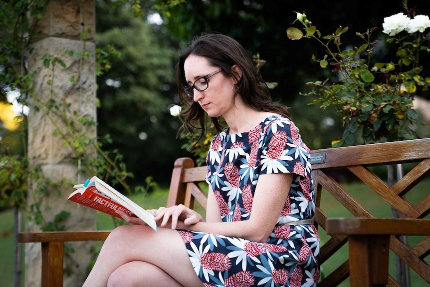 Dr Natasha Moore reads a book on a park bench.